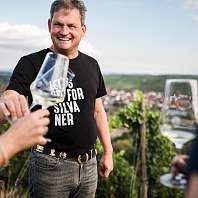 Ralph Düker mit einem Glas Weisswein vor dem Weinberg 
